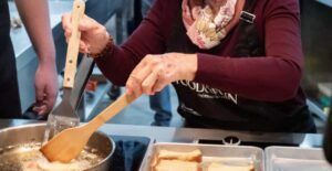 En una acogedora cocina, alguien prepara hábilmente pan y fríe con espátulas de madera. El aroma sugiere "Clase de cocina española en Valencia: tapas y vinos", ofreciendo una auténtica experiencia culinaria. - ForTwo - Planes para parejas
