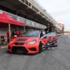 Una persona está parada junto a un auto de carreras rojo en la pista de Valencia, rodeada por un equipo de boxes dedicado, listo para Copilotaje extremo en Valencia. - ForTwo - Planes para parejas