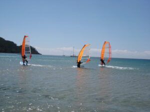 Tres personas con velas naranjas practican windsurf cerca de Atalaya Isdabe en un día soleado, mostrando sus habilidades y entusiasmo tras finalizar el Curso de Windsurf en Atalaya Isdabe. - ForTwo - Planes para parejas