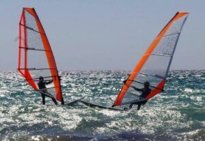 Dos windsurfistas con velas naranjas se enfrentan en el brillante océano cerca de Atalaya Isdabe, perfeccionando sus habilidades bajo un cielo azul claro, mientras participan en el Curso de Windsurf en Atalaya Isdabe. - ForTwo - Planes para parejas
