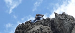 Un escalador decidido recorre con destreza una escarpada formación rocosa, que recuerda a las desafiantes rutas presentadas en el Curso de escalada y rappel en Alange, contra un cielo azul intenso. - ForTwo - Planes para parejas