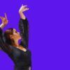 Con un vestido de encaje negro y brazos levantados, una mujer encarna el espíritu del baile flamenco sobre un fondo morado con un borde de lunares, capturando la esencia del "Curso privado de baile flamenco en Marbella". - ForTwo - Planes para parejas