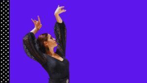 Con un vestido de encaje negro y brazos levantados, una mujer encarna el espíritu del baile flamenco sobre un fondo morado con un borde de lunares, capturando la esencia del "Curso privado de baile flamenco en Marbella". - ForTwo - Planes para parejas