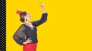 Una mujer con atuendo tradicional posa con gracia sobre un fondo amarillo con una tira de lunares, haciendo eco de un “Curso privado de baile flamenco en Marbella”. - ForTwo - Planes para parejas