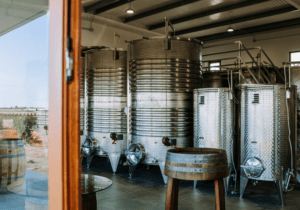 Eche un vistazo a través de una ventana de la Bodega de Menorca y descubra relucientes tanques y barriles de acero inoxidable donde se elaboran con maestría los Vinos y Vermut de Descubre. - ForTwo - Planes para parejas