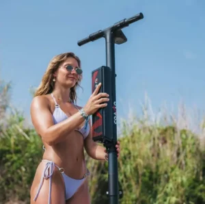 Una mujer con un bikini blanco y gafas de sol se encuentra al aire libre con un scooter eléctrico E-Paddle Surf en Marbella frente a un exuberante fondo de césped, capturando la esencia elegante de Marbella. - ForTwo - Planes para parejas