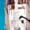 Vista aérea de un velero en las cristalinas aguas azules cerca de Formentera, con dos bañistas disfrutando de una Escapada en velero de Ibiza a Formentera cerca. - ForTwo - Planes para parejas