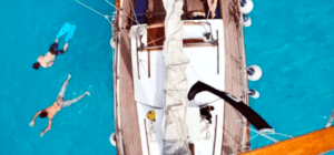 Vista aérea de un velero en las cristalinas aguas azules cerca de Formentera, con dos bañistas disfrutando de una Escapada en velero de Ibiza a Formentera cerca. - ForTwo - Planes para parejas