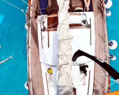 Vista aérea de un velero en las cristalinas aguas azules cerca de Formentera, con dos bañistas disfrutando de una Escapada en velero de Ibiza a Formentera cerca. - ForTwo - Planes para parejas
