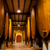 Una bodega poco iluminada con grandes barriles de madera alineados a ambos lados de un estrecho pasillo invita a una escapada gastronómica a Astigarraga. - ForTwo - Planes para parejas