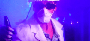 Una persona con bata y mascarilla, sosteniendo una botella de spray bajo una luz violeta vibrante, evoca la experiencia inmersiva de resolver misterios con las aventuras de Escape Room VR en Castellón. - ForTwo - Planes para parejas