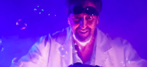 En Castellón, una persona con gafas y bata blanca irradia bajo una luz violeta rodeada de burbujas flotantes, creando una atmósfera que recuerda a la experiencia de Escape Room VR en Castellón. - ForTwo - Planes para parejas