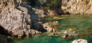 El agua turquesa cristalina, los acantilados escarpados y la escasa vegetación de la costa rocosa de Girona invitan a los aventureros a explorar con la experiencia "Escape Room en Kayak por Girona" bajo un cielo soleado. - ForTwo - Planes para parejas