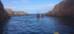 Dos kayakistas navegan entre acantilados rocosos cerca de Girona en una aventura de Escape Room en Kayak, rodeados de un mar que promete emoción bajo el inmenso cielo azul. - ForTwo - Planes para parejas
