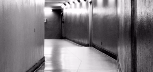 Un pasillo estrecho y poco iluminado, con paredes lisas y reflejos angulares, crea un ambiente inquietante que recuerda a "Escape room ciberataque en Bilbao". - ForTwo - Planes para parejas
