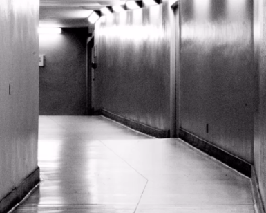 Un pasillo estrecho y poco iluminado, con paredes lisas y reflejos angulares, crea un ambiente inquietante que recuerda a "Escape room ciberataque en Bilbao". - ForTwo - Planes para parejas