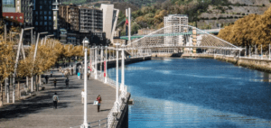 Disfruta de un pintoresco paseo junto al río en Bilbao, con un puente y arquitectura a ambos lados. Bordeado de árboles, el sendero ofrece tranquilidad en medio de la vida urbana. Mejora la experiencia con "Escape Room Ciberataque en Bilbao" y vive una emocionante aventura urbana. - ForTwo - Planes para parejas