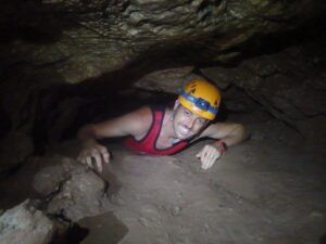 Con una camiseta roja y un casco amarillo, alguien se arrastra por el Túnel del Sumidor, disfrutando de "Espeleología acuática en el Túnel del Sumidor: una aventura extrema en pareja". - ForTwo - Planes para parejas