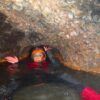 Con traje de neopreno y casco, alguien navega por la estrecha cueva llena de agua del Túnel del Sumidor, capturando la emoción de "Espeleología acuática en el Túnel del Sumidor: una aventura extrema en pareja". - ForTwo - Planes para parejas
