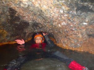 Con traje de neopreno y casco, alguien navega por la estrecha cueva llena de agua del Túnel del Sumidor, capturando la emoción de "Espeleología acuática en el Túnel del Sumidor: una aventura extrema en pareja". - ForTwo - Planes para parejas
