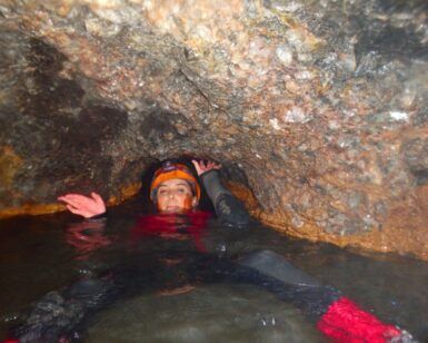 Con traje de neopreno y casco, alguien navega por la estrecha cueva llena de agua del Túnel del Sumidor, capturando la emoción de "Espeleología acuática en el Túnel del Sumidor: una aventura extrema en pareja". - ForTwo - Planes para parejas