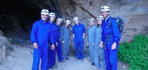 A la entrada de la cueva, un grupo de trajes azules y grises con cascos se prepara para un emocionante día de Espeleología con Rápel en Montanejos, explorando las profundidades. - ForTwo - Planes para parejas