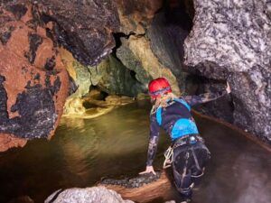 Vestido con equipo de espeleología, una persona explora un pasaje de cueva rocoso lleno de agua con una linterna frontal, abrazando la aventura de "Espeleología en Valencia: una aventura subterránea para vivir en pareja". - ForTwo - Planes para parejas