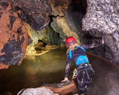 Vestido con equipo de espeleología, una persona explora un pasaje de cueva rocoso lleno de agua con una linterna frontal, abrazando la aventura de "Espeleología en Valencia: una aventura subterránea para vivir en pareja". - ForTwo - Planes para parejas