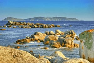 Costas rocosas con un mar azul, grandes rocas dispersas y colinas bajas distantes bajo un cielo despejado lo hacen perfecto para una "Excursión en Barco a la Isla de Ons". - ForTwo - Planes para parejas