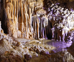 Explora las Cuevas de Génova ofrece una escena fascinante en Mallorca, con impresionantes estalactitas y estalagmitas con iluminación violácea que se refleja en aguas tranquilas, perfectas para explorar. - ForTwo - Planes para parejas