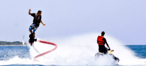 Sobre las cristalinas aguas de Alcocéber, una persona desafía con gracia la gravedad en un Flyboard en Alcocéber mientras recibe la guía experta de otra en una moto acuática. - ForTwo - Planes para parejas