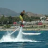 Alguien está disfrutando del Flyboard en Marbella, volando sobre el océano con el impresionante telón de fondo de las montañas y los edificios de Marbella que realzan la impresionante escena. - ForTwo - Planes para parejas