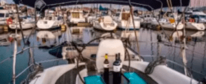 La vista desde la cubierta de un barco ofrece botellas de vino y un puerto deportivo lleno de barcos al atardecer. Es el lugar ideal para relajarse después de un día de Iniciación a la vela en Bilbao, disfrutando de la serena belleza del mar mientras reflexiona sobre su nueva pasión por la navegación. - ForTwo - Planes para parejas