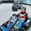 Una persona en un kart azul con casco está lista para competir en la pista de Karting en Ojén, con otros karts entusiastas alineados detrás de ella. - ForTwo - Planes para parejas