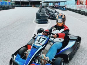 Una persona en un kart azul con casco está lista para competir en la pista de Karting en Ojén, con otros karts entusiastas alineados detrás de ella. - ForTwo - Planes para parejas