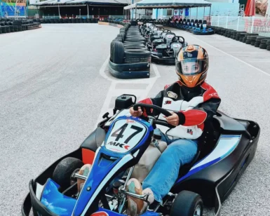 Una persona en un kart azul con casco está lista para competir en la pista de Karting en Ojén, con otros karts entusiastas alineados detrás de ella. - ForTwo - Planes para parejas