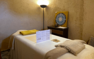 Relájese en una acogedora sala de masajes equipada con una cama, iluminación suave, mantas y un mandala decorativo en un mueble para la experiencia perfecta de Masaje Mediterráneo en Mallorca. - ForTwo - Planes para parejas