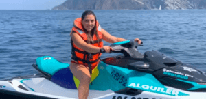 Con un chaleco salvavidas naranja, una mujer navega en la Moto de agua en Getxo sin carnet por el océano, con acantilados rocosos que crean un impresionante paisaje. ¡No se necesita carnet para esta emocionante aventura!. - ForTwo - Planes para parejas