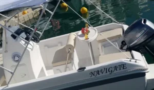 Pequeña embarcación blanca llamada NAVIGATE con motor Yamaha, asientos y mesa, amarrada en un puerto deportivo de la Costa del Sol. Ideal para disfrutar de la experiencia "Navega en Pareja por la Costa del Sol". - ForTwo - Planes para parejas