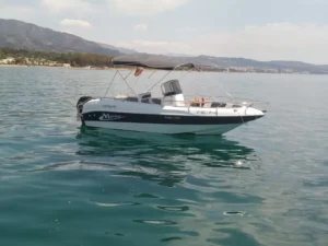 El Navega en Pareja por la Costa del Sol, un pequeño barco a motor blanco y azul, flota en las serenas aguas cerca de la hermosa costa de la Costa del Sol, con montañas distantes como un impresionante telón de fondo. - ForTwo - Planes para parejas