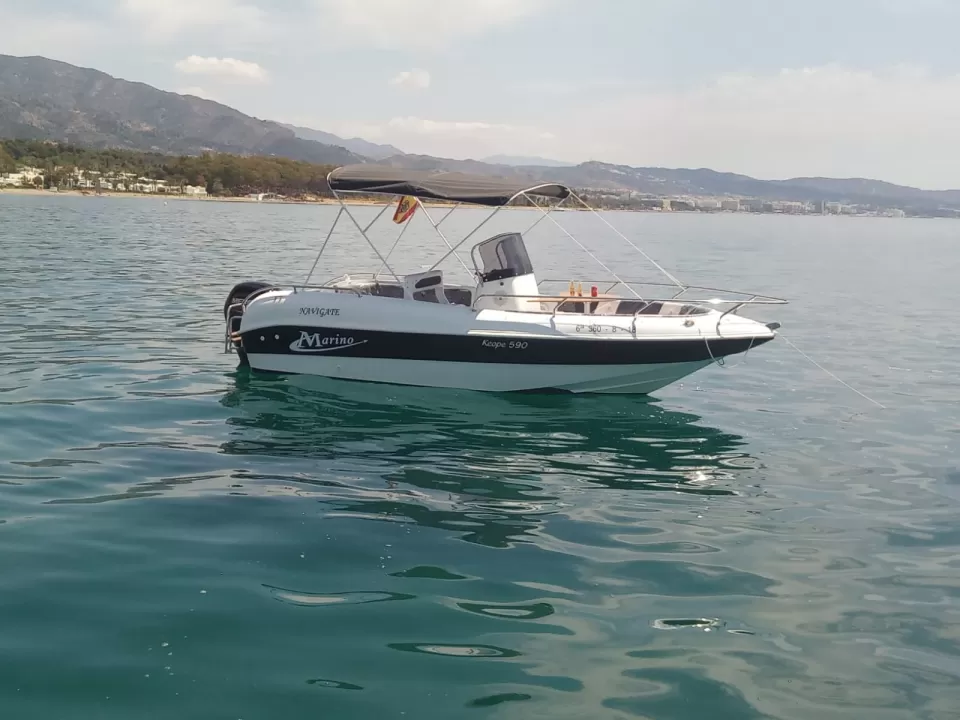 El Navega en Pareja por la Costa del Sol, un pequeño barco a motor blanco y azul, flota en las serenas aguas cerca de la hermosa costa de la Costa del Sol, con montañas distantes como un impresionante telón de fondo. - ForTwo - Planes para parejas