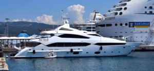 Un Yate de Lujo en Girona está elegantemente atracado cerca de un crucero en el soleado puerto, ofreciendo una Noche Romántica en sus opulentas cubiertas. - ForTwo - Planes para parejas