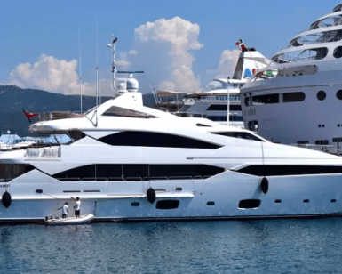 Un Yate de Lujo en Girona está elegantemente atracado cerca de un crucero en el soleado puerto, ofreciendo una Noche Romántica en sus opulentas cubiertas. - ForTwo - Planes para parejas