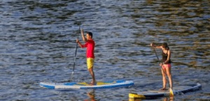 En el Embalse del Sichar, dos personas practican paddle surf, uno viste camiseta roja y pantalón corto amarillo, mientras que el otro viste ropa oscura. - ForTwo - Planes para parejas