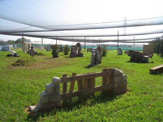 El producto "Paintball en Valencia: ¡vive la batalla definitiva!" ofrece un campo de paintball en Valencia con zonas de césped con obstáculos dispersos y barreras que simulan lápidas. - ForTwo - Planes para parejas