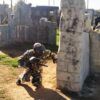 En el corazón de Valencia, alguien camuflado se agacha con una pistola de paintball tras una barrera de hormigón, inmerso en "Paintball en Valencia: ¡vive la batalla definitiva!" en un campo al aire libre. - ForTwo - Planes para parejas