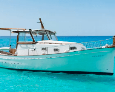 Un Paseo en Barco por la Costa de Palma está anclado en las cristalinas aguas turquesas, frente a un cielo azul brillante. - ForTwo - Planes para parejas