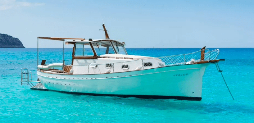 Un Paseo en Barco por la Costa de Palma está anclado en las cristalinas aguas turquesas, frente a un cielo azul brillante. - ForTwo - Planes para parejas