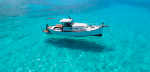 Una barca blanca de Paseo en Barco por la Costa de Palma se desliza sobre aguas cristalinas y turquesas proyectando una sombra sobre el fondo marino. - ForTwo - Planes para parejas