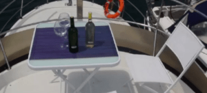 Un paseo en barco romántico por Bilbao cuenta con una mesa blanca y sillas en la cubierta con dos botellas de vino y copas, creando el ambiente romántico perfecto, completo con un salvavidas en el fondo. - ForTwo - Planes para parejas